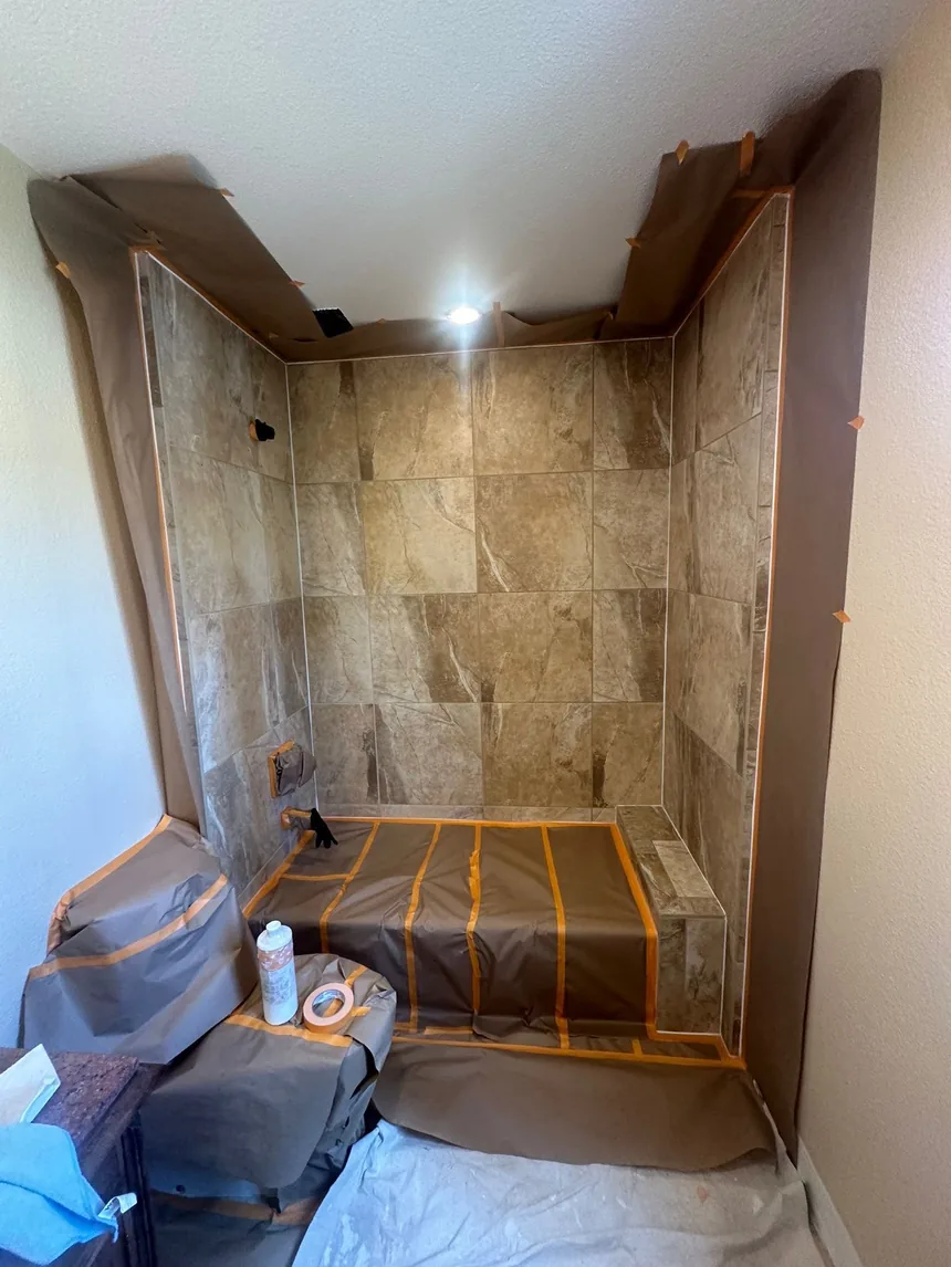 A shower alcove tiled in brown travertine-effect tile, masked off with paper and tape ready for spraying.