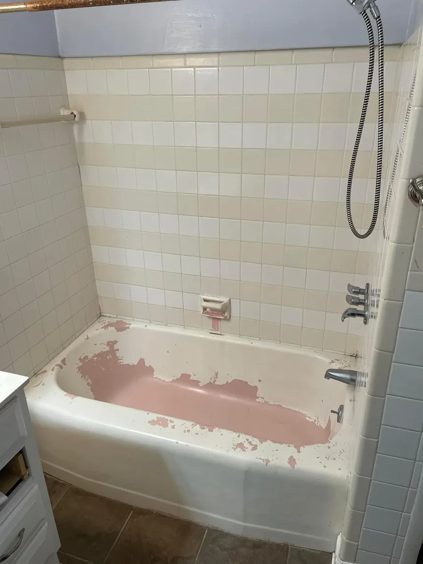 A bathtub with peeling pink coating and yellowed tile before refinishing.