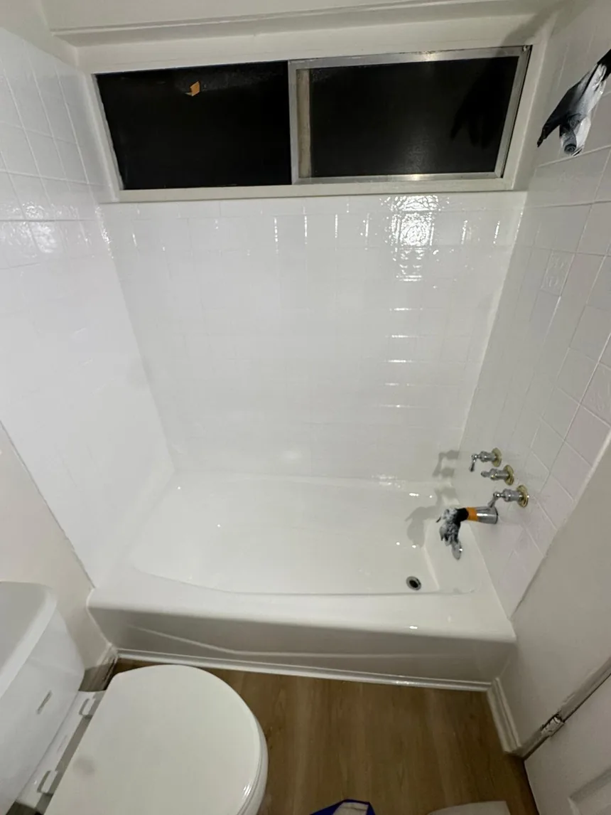 A tiled wall refinished in one even white, with the bathtub below it.