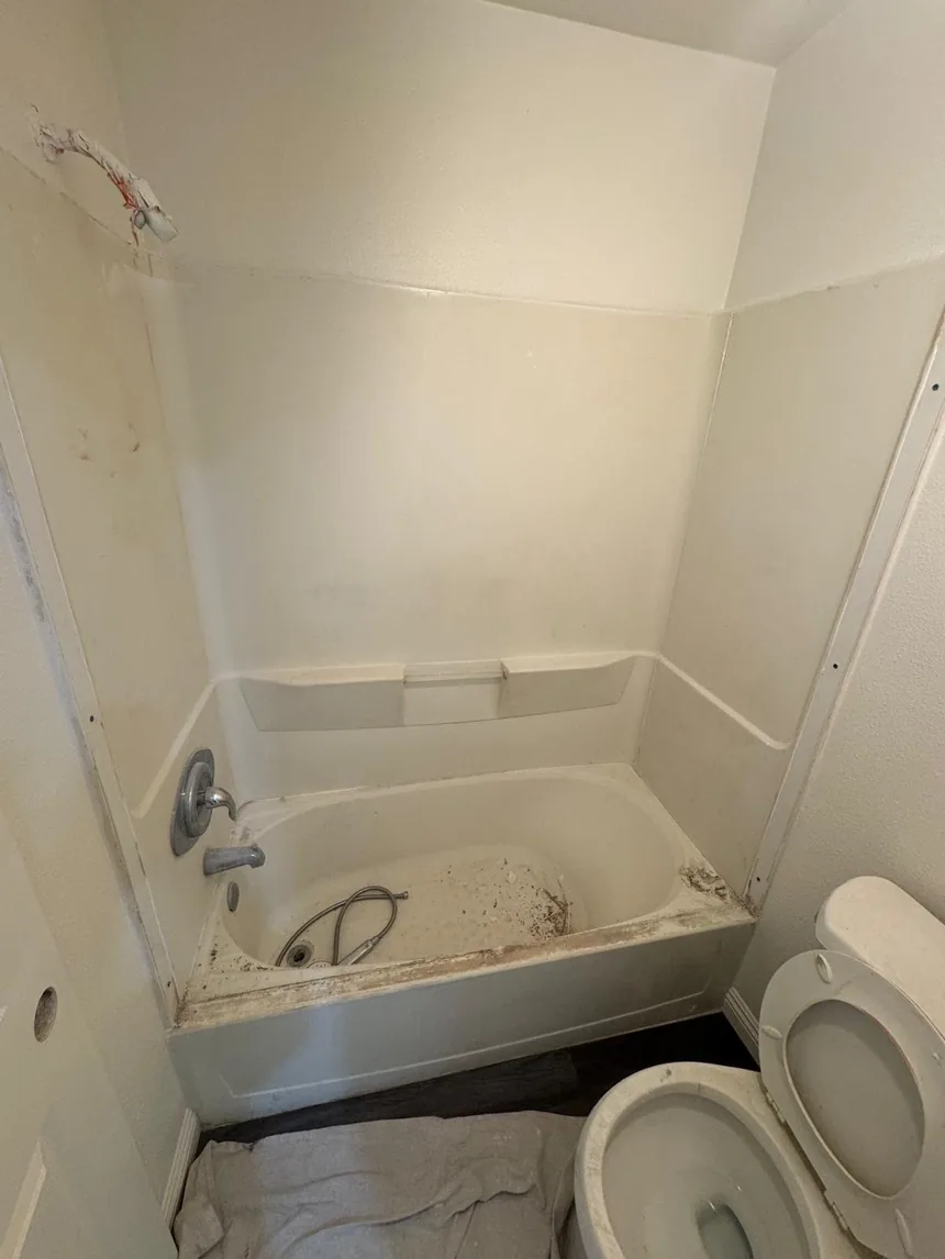 A one-piece fibreglass tub and surround, yellowed with black staining along the tub line.