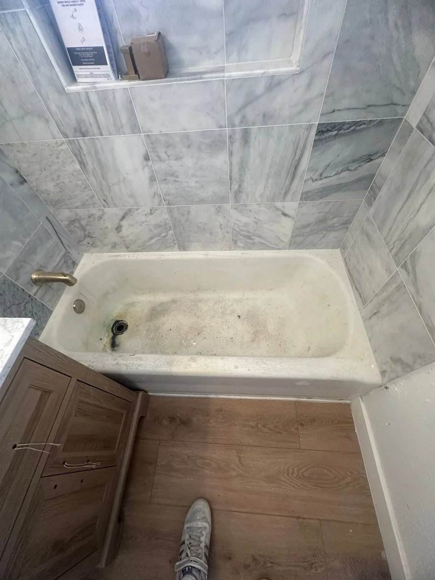 A stained bathtub in a marble-tiled bathroom before refinishing.