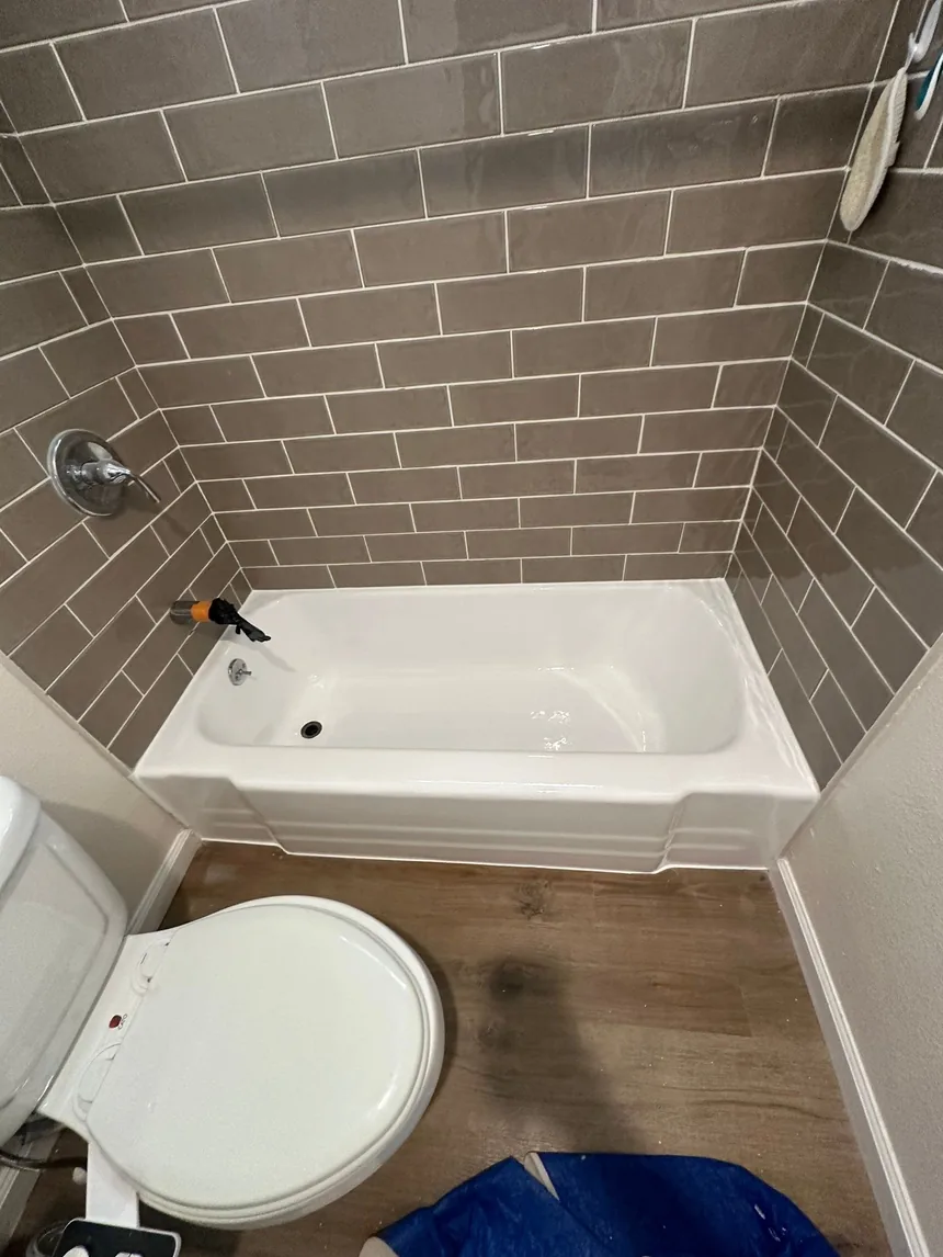 The same bathtub refinished in gloss white against the gray subway tile, everything unmasked and clean.