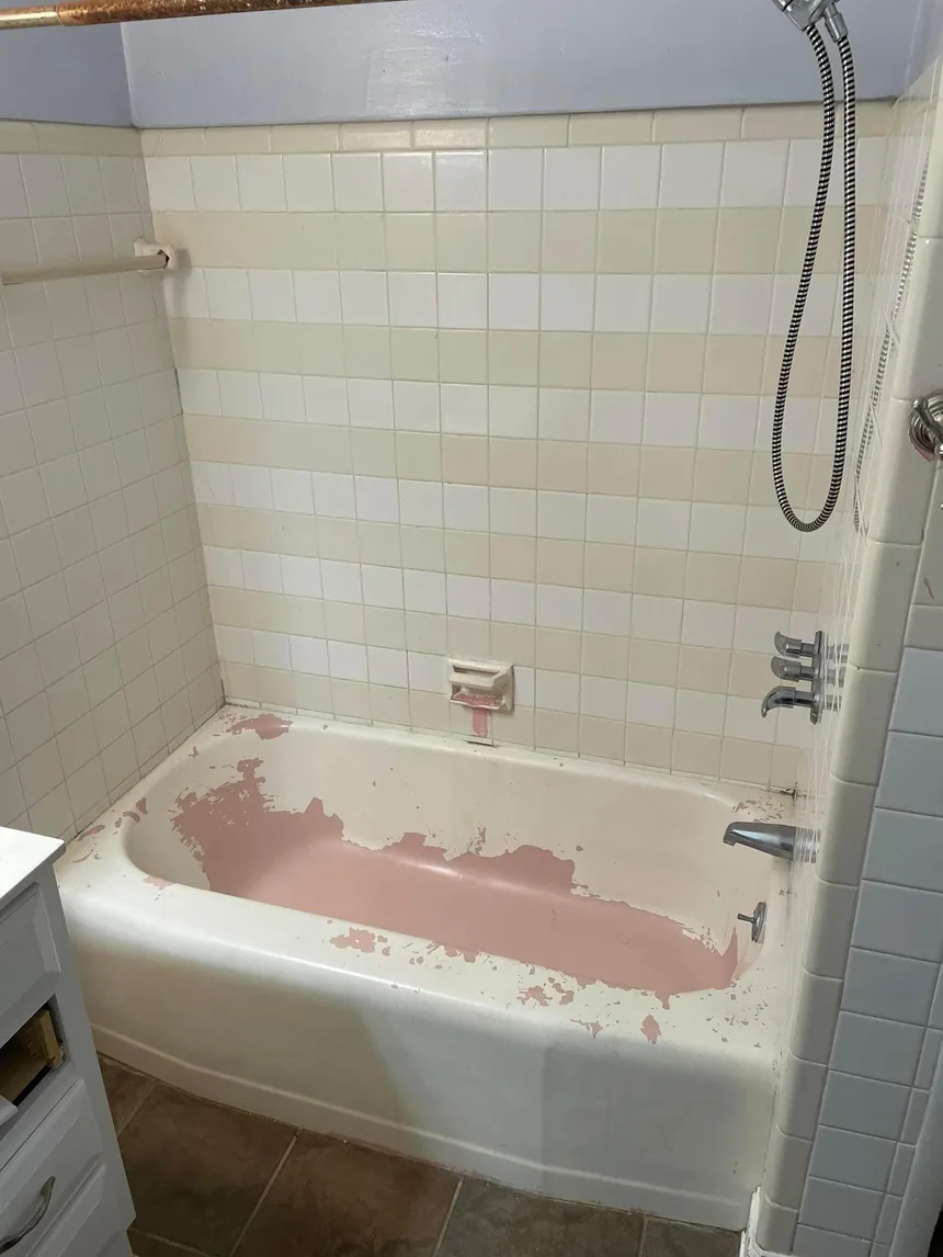 A bathtub where a white coating has worn away across the base, showing the original pink surface underneath.