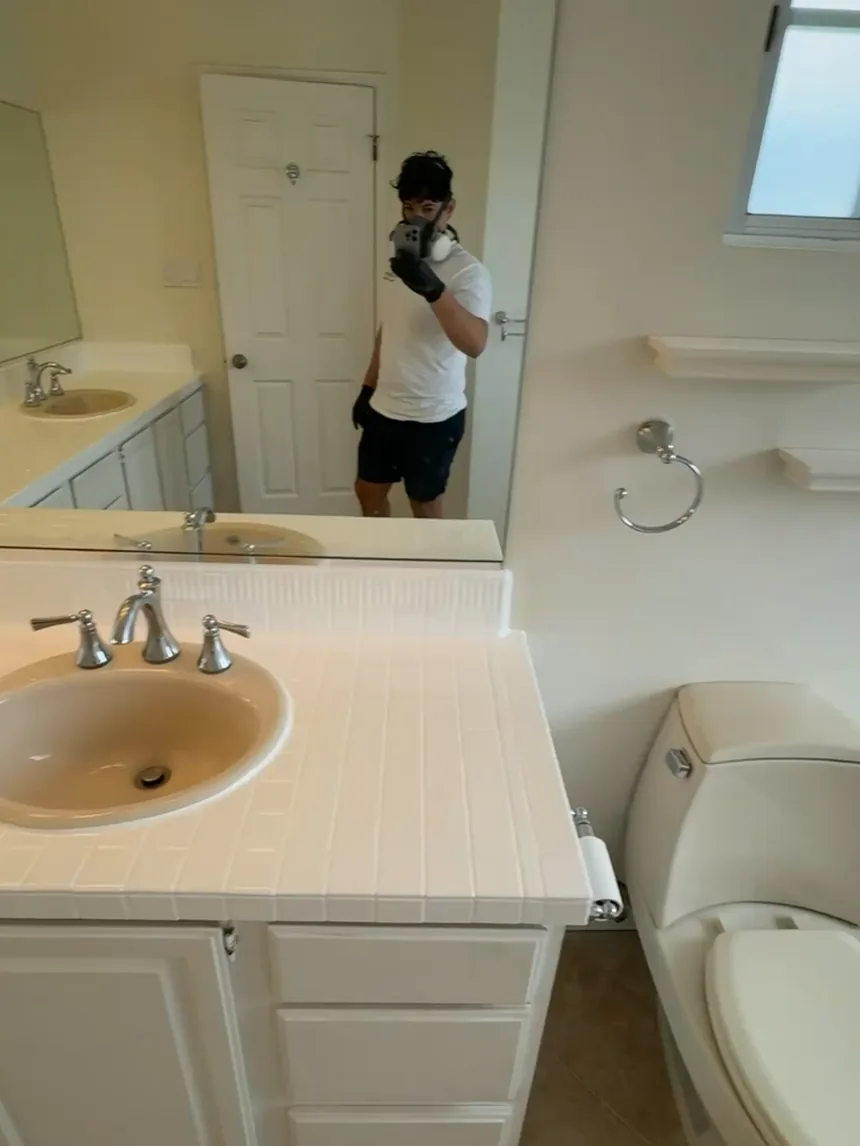 A refinished sink and tile counter, with the person who did the work reflected in the mirror wearing a respirator.