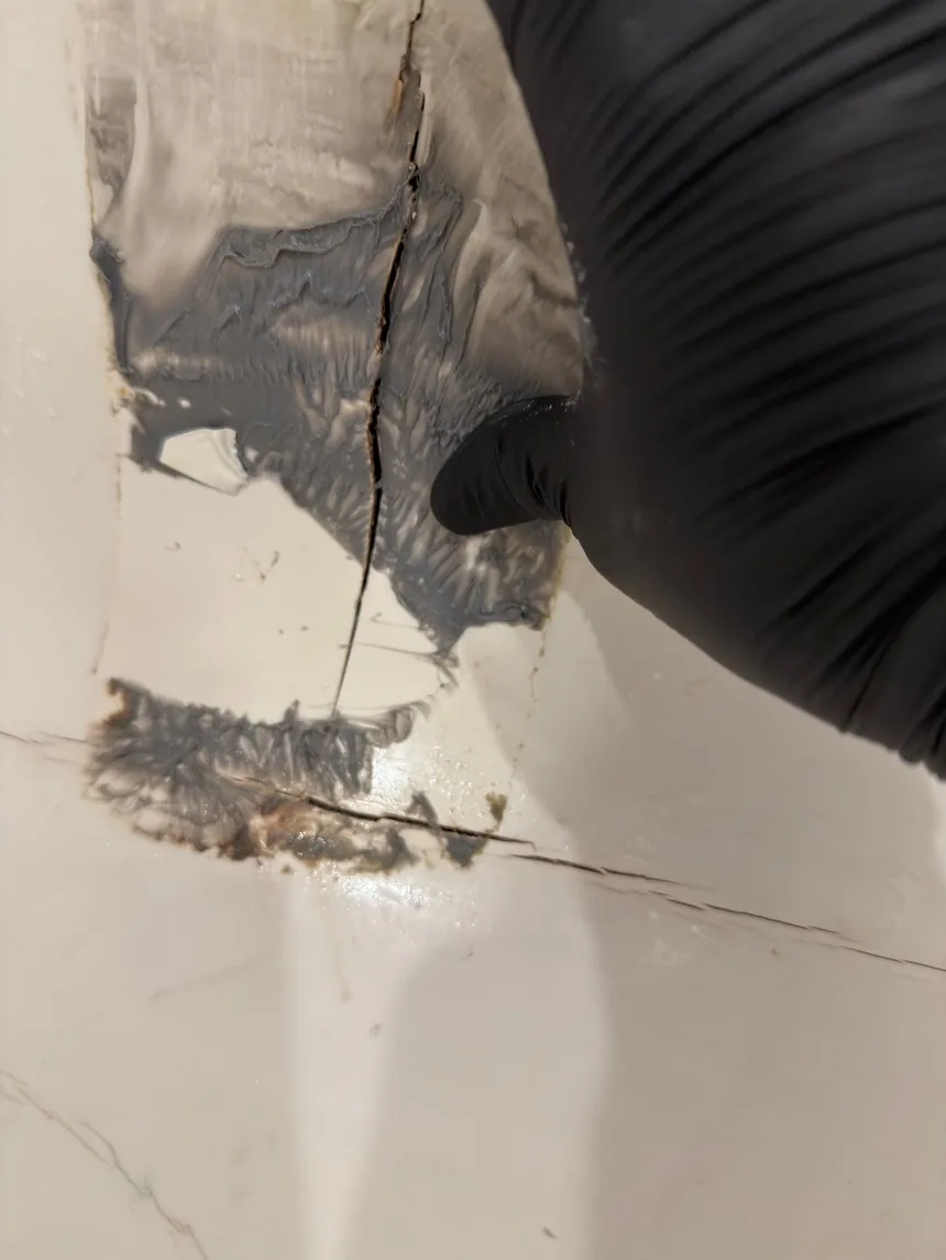 A gloved hand pressing filler into a crack running across the rim of a bathtub.