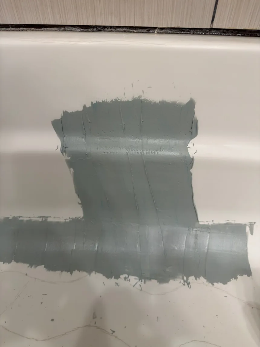 Filler spread along the damaged edge of a bathtub, waiting to be sanded flat.