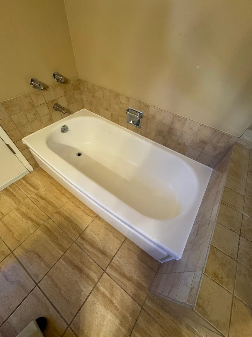 A refinished white bathtub against the original tan tile it sits in.